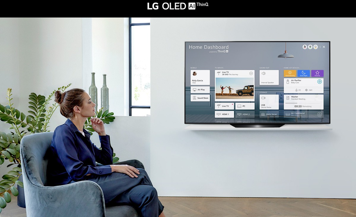 O femeie care stă pe un scaun în camera de zi, cu Home Dashboard pe ecranul TV